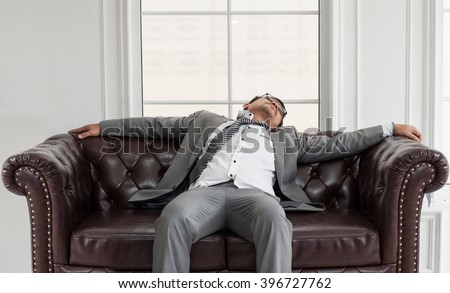 Businessman exhausted and tired from overtime working, He sit and sleep on brown leather sofa.