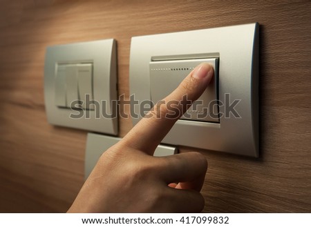 A finger is turning on a grey metallic light switch.