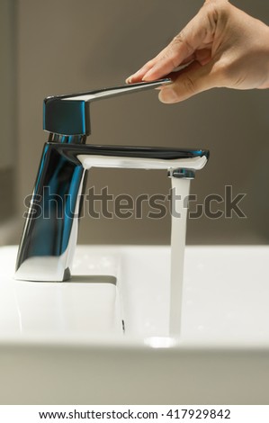 Close up of Hand with faucet and water flow on vanity basin in the bathroom.