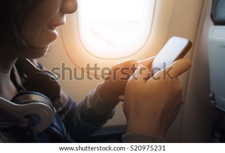 Happiness of Asian girl with headphone using smartphone and smiling on the airplane.