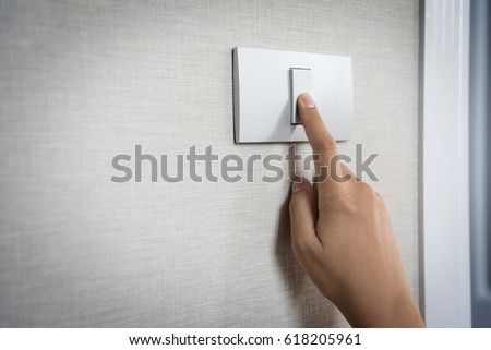 Close up hand turning on or off on grey light switch with texture background. Copy space.