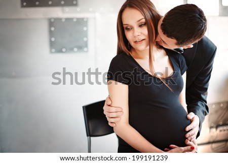 Man kissing his pregnant wife on the neck. Beautiful and elegant man and woman. Young family.