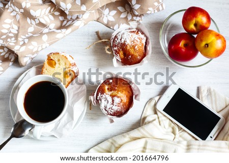 Fresh breakfast with muffins in paper cupcake holders, coffee and fruits (peach and nectarine). Phone for social media and morning news.