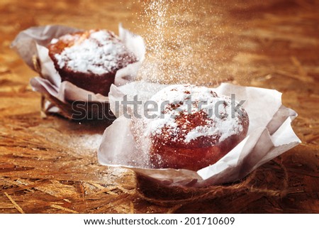 Fresh muffins with pouring sugar powder in paper cupcake holders. Selective focus. Close up.
