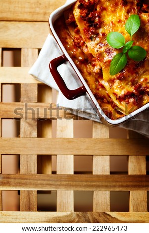 Italian Food. Hot tasty Lasagna plate served with fresh basil leaf. Wooden table background. Top view, space for your text.