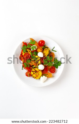 Grilled vegetables with mozzarella cheese. Cherry tomatoes, pepper, eggplant, zucchini served with parsley in white plate on white background with fresh herbs. Top view.