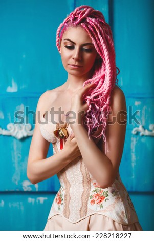 Freaky young female model in vintage corset with rose flower decoration on rusty blue tourqoise background. Bright pink dreadlocks hairstyle, beauty make up.