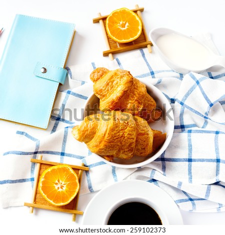 Breakfast concept. Coffee and oranges and fresh baked tasty croissant on white background. Personal diary for successful day. Top view, selective focus.