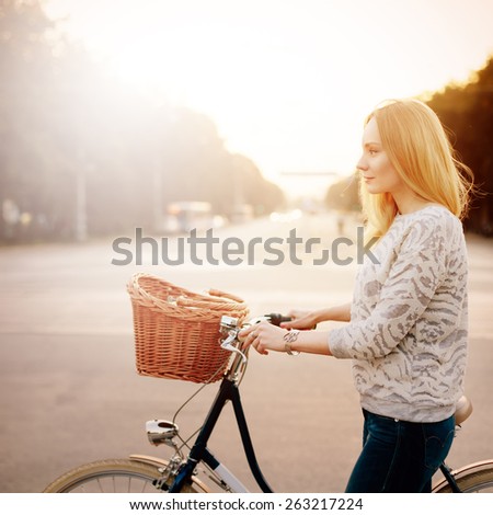 Young blonde woman on a vintage bicycle in the sunset. Image toned in instagram style. Selective focus. Shallow DOF.