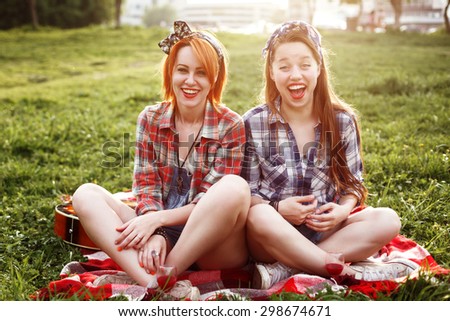 Two Young Laughing Hipster Women in Pin Up Style Having Fun at a Picnic in the Park in the Sunset