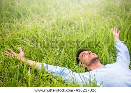 Happy beautiful man lying on the green grass with arms outstretched