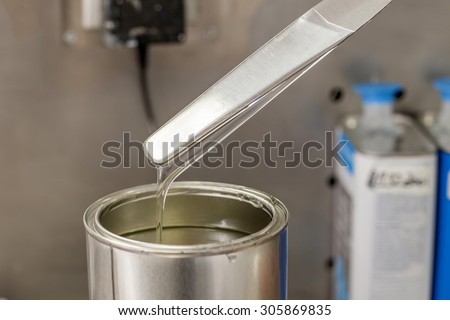 Technician weighing paint resin in a can on a balance by spatula