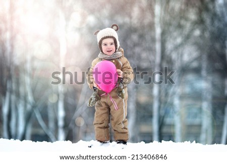boy in a knitted hat with ears and a pink balloon on a background of a winter landscape