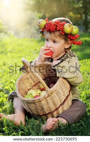 Cute boy wearing a crown of fruit with a basket of apples biting an apple