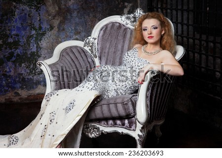 beautiful red-haired girl in evening dress sitting in a luxury lounging chair against the dark interior