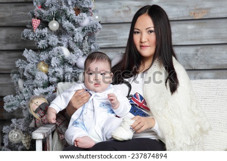 Mother with baby in her arms on the background of Christmas tree in a rustic interior