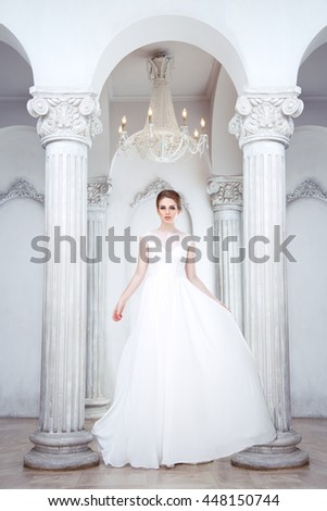 Beautiful bride in full growth in long flowing dress in the hall with columns