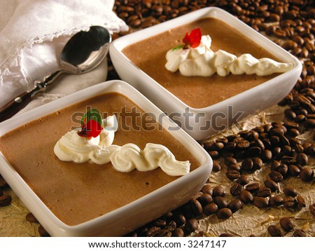 Two coffee mousse desserts, with a touch of whipped cream on top and a little red flower, on a coffee beams background
