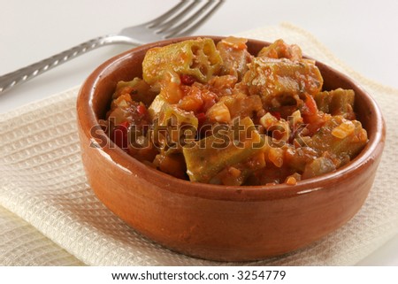 A recipe of okras (gumbos, Bamias) in mediterranean tomato\'s sauce with garlic, onion, chili, etc. with fork and napkin