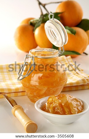 bottle with orange jam, plate, knife and fresh oranges on back, soft focus