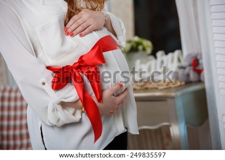belly of a pregnant woman tied with a red ribbon \
 tum and red bow \
 Pregnant woman embracing her soft tummy