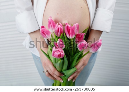 Pregnant woman embracing her belly delicate bouquet of pink tulips in the hands of pregnant girl beautiful bouquet of spring flowers bouquet of tulips at the belly of a young pregnant girl