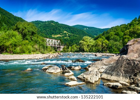 shore of a mountain river with stones and iron bridge