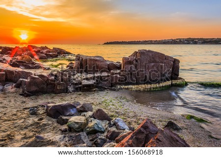 landscape red sun rise over the sea on the sandy beach with rocks and seaweed