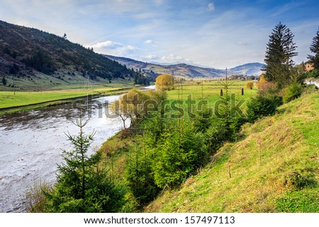 fields and trees along the river which flows at the foot of the mountains in autumn landscape