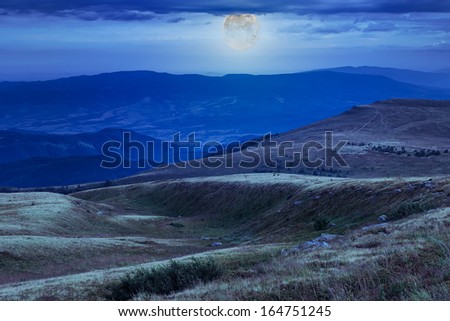 mountain landscape. valley with stones on the hillside. forest on the mountain under the moon light falls on a clearing at the top of the hill.