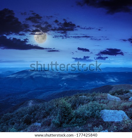 mountain landscape. valley with stones on the hillside. forest on the mountain under the moon light falls on a clearing at the top of the hill at night.
