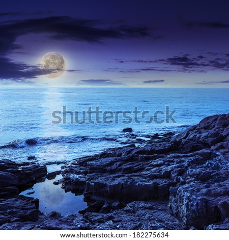 sea wave attacks the boulders and is broken about them at night in moon light