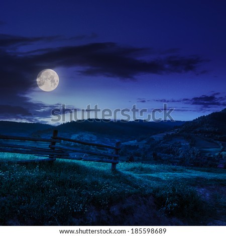 wooden fence in the grass on the hillside near the village at night in moon light