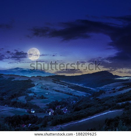 Stack of hay on a green meadow in the mountains under a blue summer sky at night in moon light