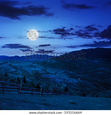 summer landscape. fence near the meadow on hillside. forest in fog on the mountain at night in moon light
