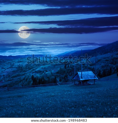 summer landscape. storage of firewood by the fence near the meadow on the hillside. forest in fog on the mountain at night in moon light