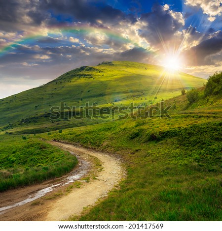 summer landscape. mountain path through the field turns uphill to the sky at sunset with rainbow