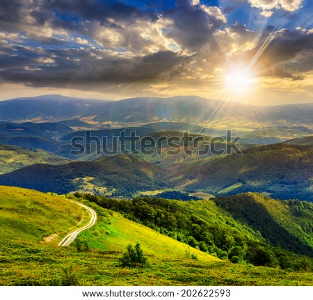 mountain range summer landscape. valley with stones and road on the hillside. forest on the mountain under the beam of light falls on a clearing at the top of the hill at sunset