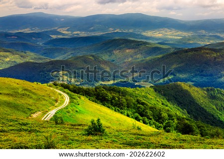 mountain range summer landscape. valley with stones and road on the hillside. forest on the mountain under the beam of light falls on a clearing at the top of the hill.