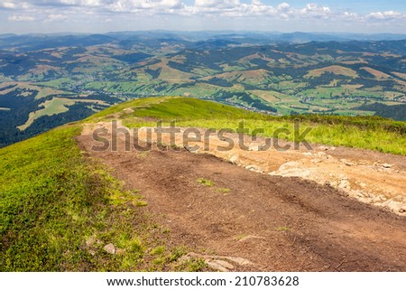 summer mountain landscape. meadow path on the hillside. forest and village on far mountain range
