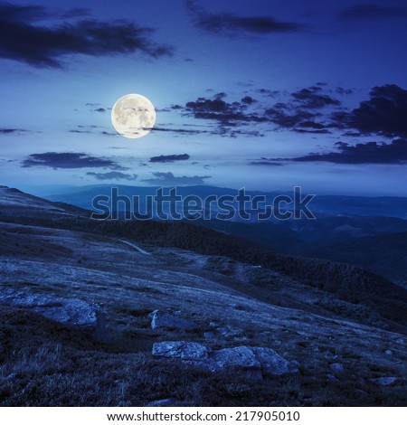 mountain landscape. valley with stones on the hillside. forest on the mountain under the full moon  light falls on a clearing at the top of the hill at night