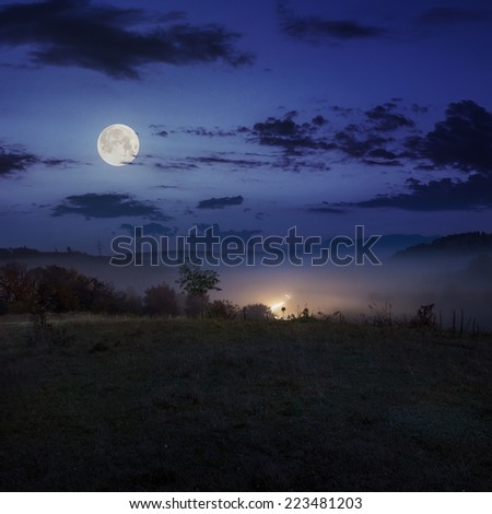 car lights in cold morning fog before  sunrise near the village in mountains  in autumn at night in full moon light