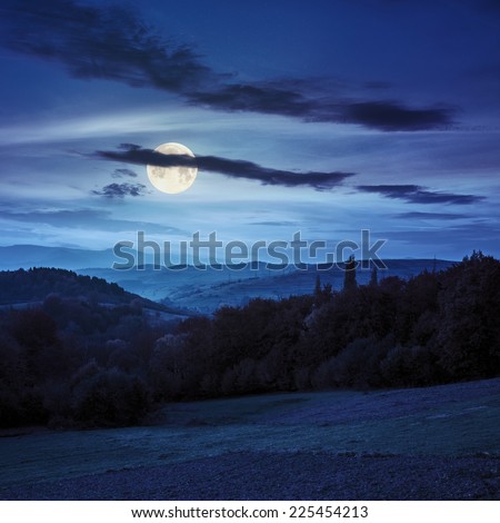 autumn landscape. village on the hillside behind forest on the mountain at night in fool moon lighy