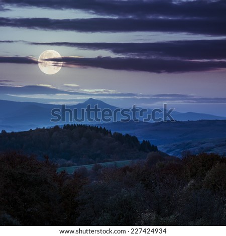 autumn landscape. yellow trees near green meadow in foggy mountains at night in full moon light