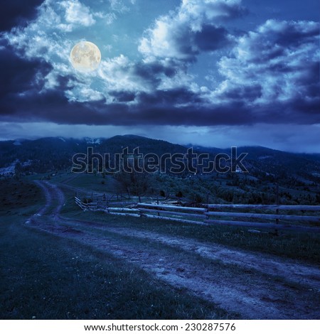 summer landscape. fence near the meadow path on the hillside. forest in fog on the mountain  at night in full moon light
