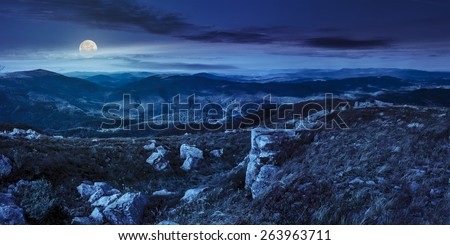 mountain panorama landscape. valley with stones in grass on top of the hillside of mountain range at night in full moon light