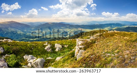 mountain panorama landscape. valley with stones in grass on top of the hillside of mountain range in dappled light