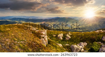 mountain panorama landscape. valley with stones in grass on top of the hillside of mountain range in sunset light