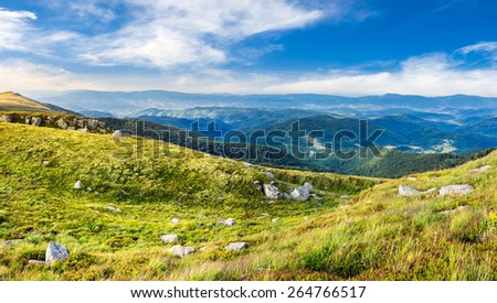 mountain landscape. valley with stones in grass on top of the hillside of mountain range in dappled light