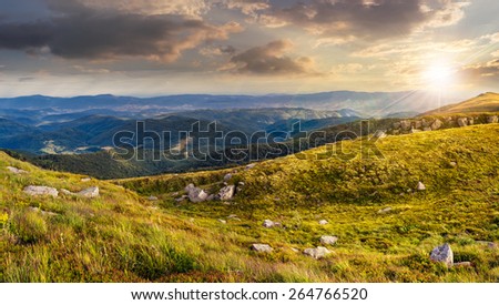 mountain landscape. valley with stones in grass on top of the hillside of mountain range in dappled sunset light